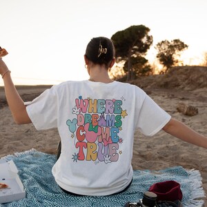May include: A white t-shirt with the text "Where Dreams Come True" in colorful letters. The shirt is decorated with stars and a Mickey Mouse silhouette.