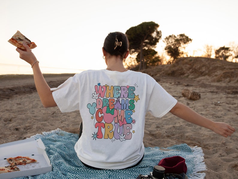 May include: A white t-shirt with the text "Where Dreams Come True" in colorful letters. The shirt is decorated with stars and a Mickey Mouse silhouette.