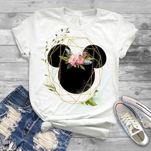 May include: White t-shirt with a black and gold geometric design featuring Mickey Mouse ears with pink flowers and green leaves.