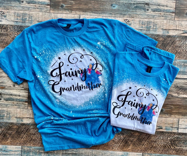 May include: Two blue t-shirts with a white bleach design. The design features a fairy godmother with a wand and the text "Fairy Godmother".