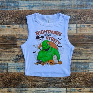 May include: White sleeveless crop top with a graphic print of the character Jack Skellington from the movie "The Nightmare Before Christmas". The graphic also includes the text "Nightmare on Main Street" and a Mickey Mouse head.
