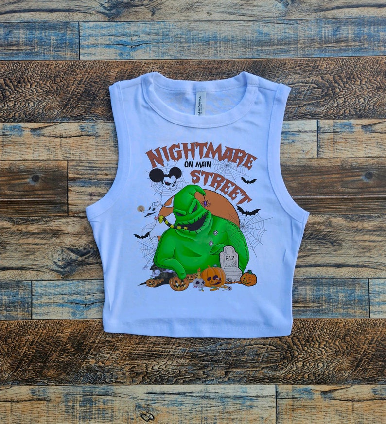 May include: White sleeveless crop top with a graphic print of the character Jack Skellington from the movie "The Nightmare Before Christmas". The graphic also includes the text "Nightmare on Main Street" and a Mickey Mouse head.