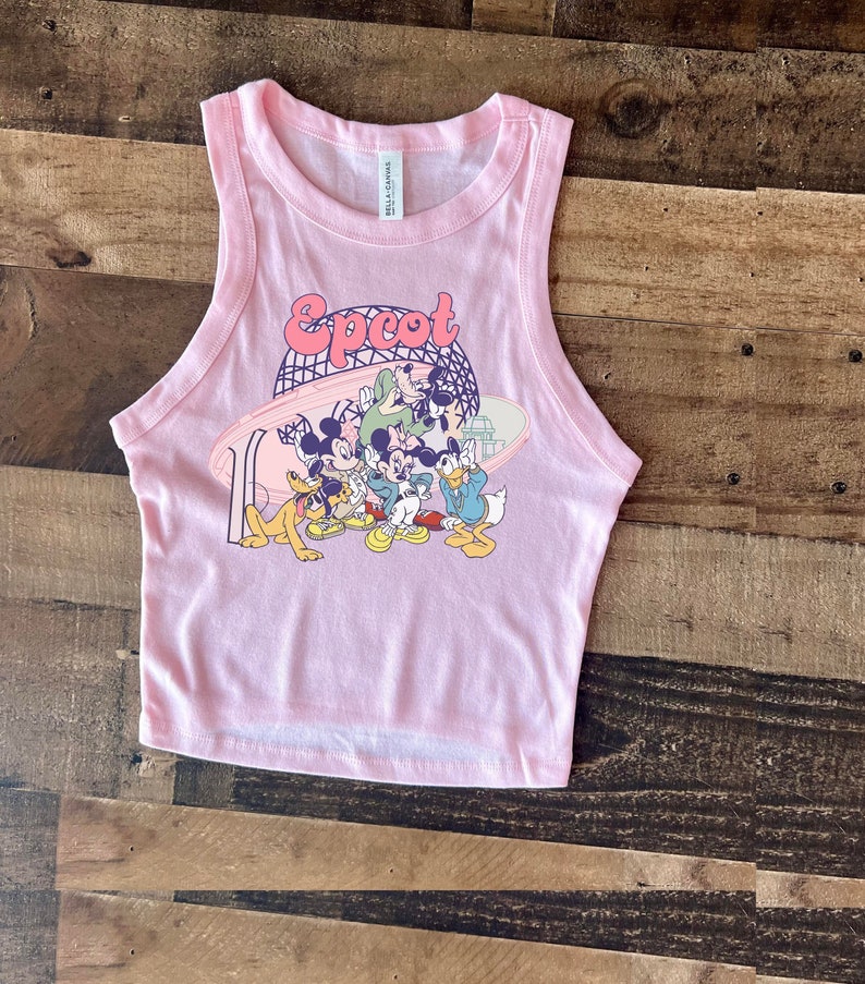 May include: A light pink tank top featuring the word "Epcot" in a retro font, with a graphic of Mickey Mouse, Minnie Mouse, Donald Duck, Goofy, and Pluto. The tank top is made of a soft material.