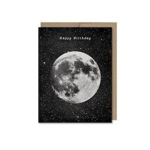 May include: A black and white greeting card with a full moon and stars in the background. The text "Happy Birthday" is printed in the top center of the card.