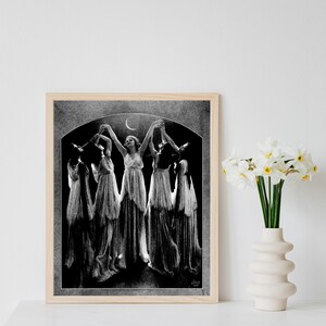 May include: Black and white photograph of five women in long dresses dancing under a crescent moon. The women are silhouetted against a dark background.