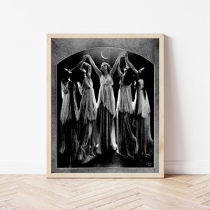 May include: Black and white vintage photograph of five women in flowing robes dancing under a crescent moon. The image has a grainy texture and is framed in a wooden frame.