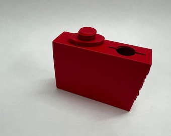 May include: A red plastic block with a round hole and a small red knob on top. The block has a textured side.
