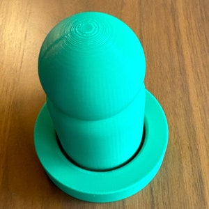 May include: A bright green plastic lidded container with a smooth, rounded top and a flat base.