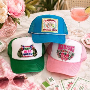 May include: Three trucker hats with mesh backs. The blue hat features a Mahjong Social Club patch and rhinestone trim. The white and green hat displays a Bam Bird Queen patch. The white and pink hat shows a Mahjong patch with a pink bow.