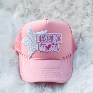 Puede incluir: Gorra de camionero rosa con una estrella blanca y un parche rosa que dice "DANCE mom" con un corazón rosa.