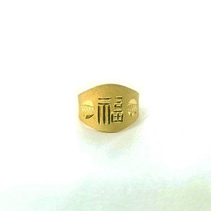 May include: A gold ring with a raised design featuring Chinese characters. The ring is wide and has a slightly curved shape.