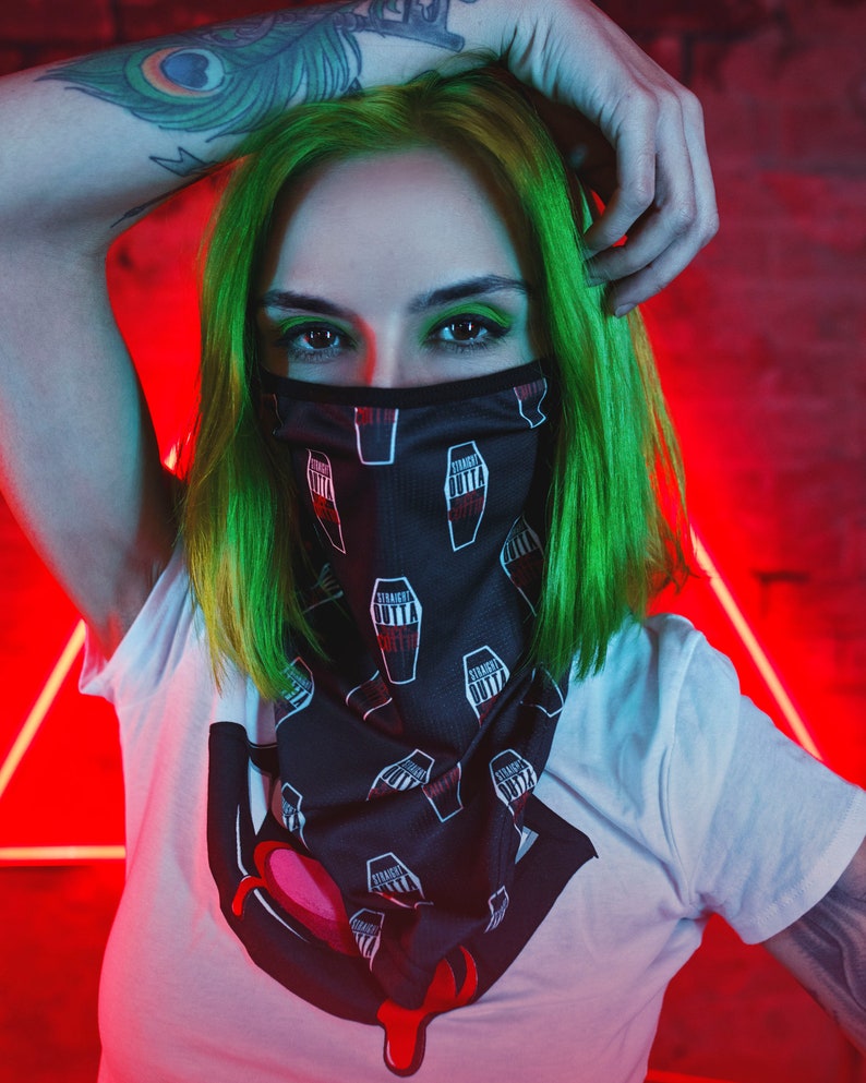 K&ouml;nnte beinhalten: Eine Person mit gr&uuml;nen Haaren tr&auml;gt ein schwarz-wei&szlig;es Bandana mit einem sich wiederholenden Muster aus S&auml;rgen und dem Text "Straight Outta". Das Bandana bedeckt Mund und Nase der Person. Die Person tr&auml;gt ein wei&szlig;es T-Shirt mit einer roten und schwarzen Grafik eines tropfenden Herzens. Die Person hat ein Tattoo eines Pfauenfeders auf ihrem Arm.