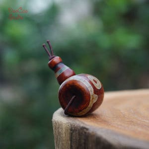 Peut inclure: Une perle d'agate brune et blanche avec un cordon brun foncé attaché. La perle présente un motif unique de lignes et de cercles blancs.