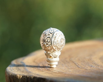 May include: A silver decorative ornament with an intricate floral design. The ornament is shaped like a sphere and has a small base.