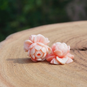 Peut inclure: Deux perles de corail rose en forme de fleur avec des sculptures complexes. Les perles sont sur une surface en bois.