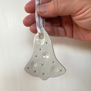 May include: White ceramic bell ornament with a snowflake design and a white satin ribbon.