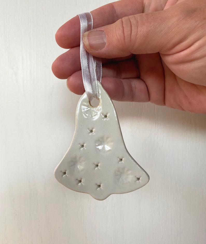May include: White ceramic bell ornament with a snowflake design and a white satin ribbon.