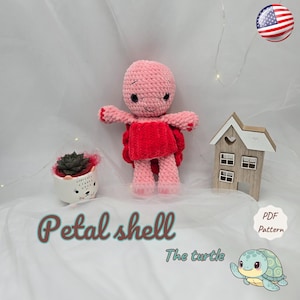 May include: A handmade pink and red crochet turtle doll with the text "Petal shell" and "The turtle". The turtle has a red shell and is standing on a white surface. A small house and a succulent in a pot are also in the image.
