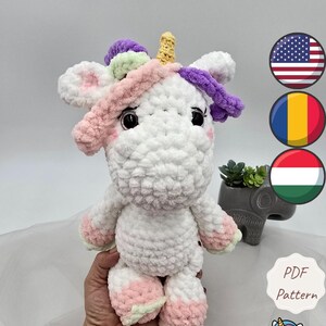 May include: A handmade, white crochet unicorn with pink, purple, and yellow accents. The unicorn has a fluffy texture and is holding a small, gray elephant-shaped planter. The text "Cotton Candy The unicorn" is visible.