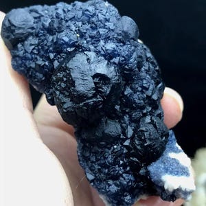 May include: A cluster of deep blue fluorite crystals with a black, iridescent sheen. The crystals are clustered together in a rough, natural formation.