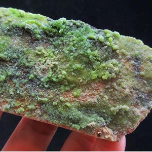 May include: A rough-hewn, irregularly shaped mineral specimen. The surface is primarily a mottled green, with areas of lighter, crystalline formations. Hints of brown and black are visible within the stone, creating a textured appearance. The overall aesthetic suggests a natural, earthy product.