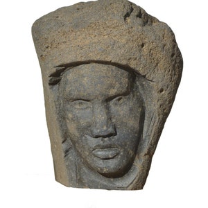 Pode incluir: Uma escultura de pedra de um rosto com uma superfície áspera e texturizada. O rosto é esculpido em detalhe, com um nariz proeminente e olhos definidos.