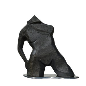Könnte beinhalten: Eine schwarze Steinskulptur eines weiblichen Torsos, ohne Kopf, in einer knienden Pose. Die Skulptur steht auf einem schwarzen Sockel.