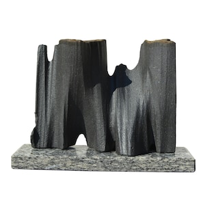 Puede incluir: Una escultura abstracta gris oscuro con una superficie texturizada, montada sobre una base rectangular de granito. La escultura tiene una forma orgánica única con múltiples picos y valles, creando un efecto visual dramático.