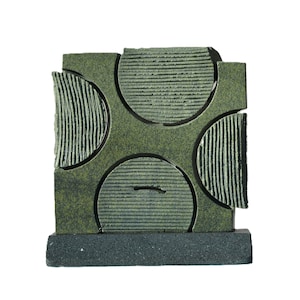 Puede incluir: Una escultura de cerámica verde con un diseño geométrico que presenta cuatro recortes circulares. La escultura tiene una superficie texturizada y está montada sobre una base negra.