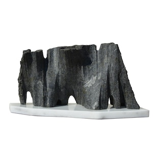 Puede incluir: Una escultura de piedra negra de una cordillera sobre una base de mármol blanco.