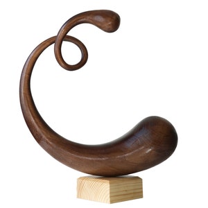 May include: A dark brown wooden sculpture of a curved, abstract shape with a small, square wooden base.