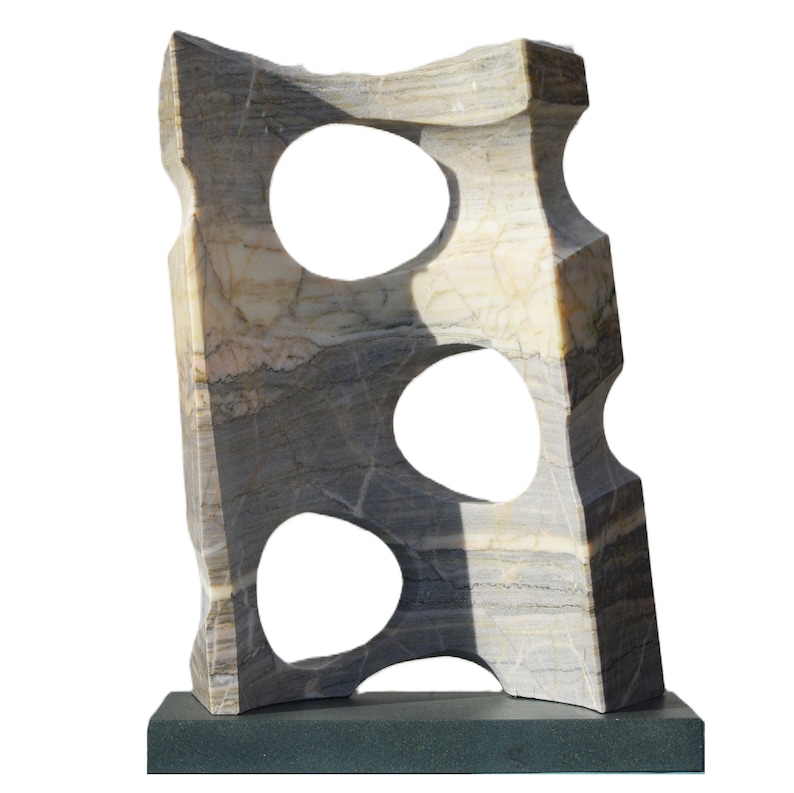 K&ouml;nnte beinhalten: Abstrakte Steinskulptur mit drei ovalen Aussparungen. Die Skulptur besteht aus grauem, beigem und wei&szlig;em Marmor und ist auf einem dunkelgrauen rechteckigen Sockel montiert. Der Stein hat nat&uuml;rliche Maserungen und eine strukturierte Oberfl&auml;che.