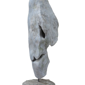 Puede incluir: Una escultura de piedra gris de forma abstracta, montada sobre una base de madera. La escultura tiene una superficie rugosa y texturizada y parece estar tallada en una sola pieza de piedra.