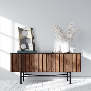 K&ouml;nnte beinhalten: Ein moderner Holzschrank mit vertikalen Holzpaneelen und schwarzen Metallbeinen. Der Schrank tr&auml;gt eine Steinskulptur mit kreisf&ouml;rmigen Ausschnitten, eine wei&szlig;e Vase mit getrockneten Blumen und andere dekorative Gegenst&auml;nde.