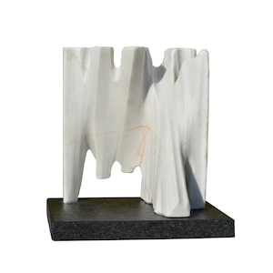 Puede incluir: Escultura abstracta de mármol blanco sobre una base negra.