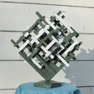 Puede incluir: Una escultura abstracta verde y blanca hecha de bloques rectangulares apilados. La escultura está sobre una base verde y se muestra sobre una superficie azul.