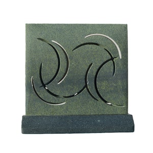 May include: A square, green sculpture with a textured surface and curved cutouts. The sculpture sits on a dark grey rectangular base. The cutouts create a flowing, abstract design. The overall aesthetic is modern and minimalist.