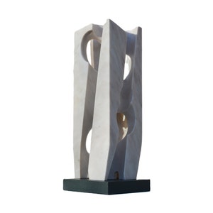 May include: A white marble sculpture with a geometric design. The sculpture has a rectangular shape with curved edges and circular cutouts. It is mounted on a dark green rectangular base. The sculpture is a modern art piece.