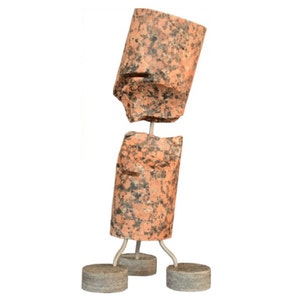 Puede incluir: Una escultura hecha de dos piezas de granito rosa, conectadas por una varilla de metal. La escultura está de pie sobre tres patas de metal con bases circulares.