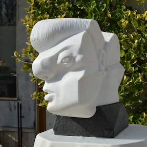 Puede incluir: Escultura de mármol blanco de la cabeza de una persona con un diseño geométrico. La escultura está sobre una base negra.