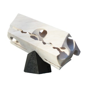 May include: A white marble sculpture with a jagged, broken design. The sculpture is mounted on a black triangular base.