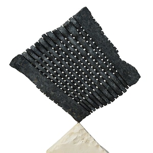 Puede incluir: Escultura abstracta. Estructura gris oscuro, similar a una rejilla con pequeños cuadrados blancos, montada sobre una base triangular de piedra blanquecina. La escultura tiene una superficie texturizada.