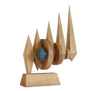 May include: A wooden sculpture with a blue geometric shape in the center. The sculpture is made of multiple pieces of wood that are arranged in a geometric pattern. The sculpture is mounted on a wooden base.