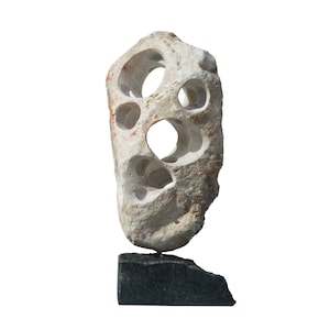 Puede incluir: Una escultura de piedra blanca con varios agujeros tallados en ella. La escultura está sentada sobre una base de piedra negra.