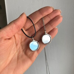 May include: Two silver necklaces with round mirror pendants. One necklace has a black cord and the other has a silver chain.