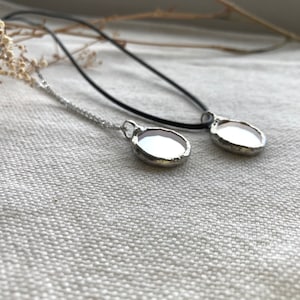 May include: Two silver necklaces with round, clear glass pendants. The necklaces are on a white fabric background.