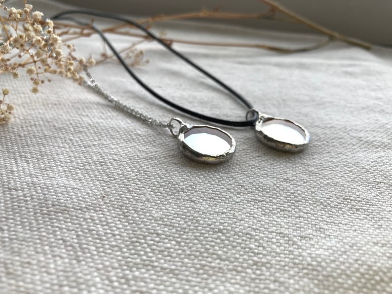 May include: Two silver necklaces with round, clear glass pendants. The necklaces are on a white fabric background.