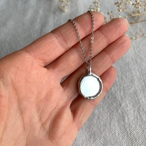 May include: A silver chain necklace with a round, silver pendant. The pendant has a smooth, reflective surface.