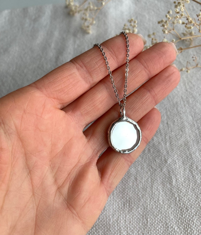 May include: A silver chain necklace with a round, silver pendant. The pendant has a smooth, reflective surface.