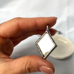 May include: A silver diamond-shaped pendant with a mirror inside. The pendant is hanging from a silver chain.